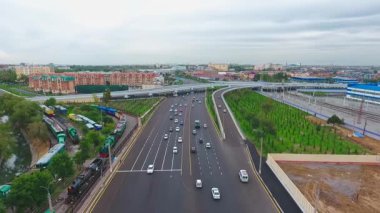 İnsansız hava aracı hareket halindeki arabalarla şehrin yollarında ve otoyollarında uçuyor. Bulutlu bir yaz günü. Hava Görünümü.