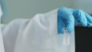 Laboratuvarda cam eşyalar ile çalışan koruyucu giysili laboratuvar teknisyenlerinin elleri. Kapat, Yavaş Hareket.