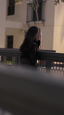 Saçları rüzgarda uçuşan, akşam yürüyüşünde uzun bir yağmurlukla genç bir kadın. Yavaş Hareket