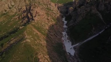Bir dron buzla dağ geçidinde uçuyor. Etrafta ağaçlar ve çalılar var. Güneşli bir bahar günü. Hava Görünümü