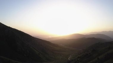 Batan güneşin aydınlattığı yeşil dağların üzerinde bir dron uçuyor. Hava Görünümü.