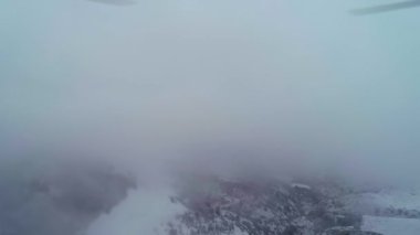 İnsansız hava aracı karla kaplı dağların üzerinden bulutların üzerinden uçuyor. Bulutlu bir kış günü. Hava Görünümü.