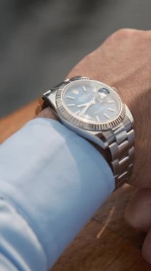 Dubai, BAE - 114 2023: Lüks kol saati olan iş elbiseli genç bir adam pahalı bir premium arabanın yanında duruyor. Dubai 'de bulutlu bir akşam. Kapat, Yavaş Hareket