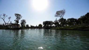 Ağaçlarla çevrili bir parktaki göl suyunda bir dron. Güverte köprüsünün manzarası. Bulutsuz bir yaz günü. Hava Görünümü
