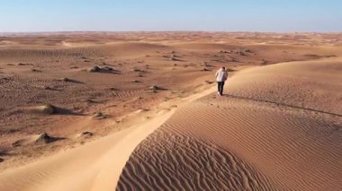 Çölde kumulda yürüyen yalnız bir adamın üzerinde bir dron. Dubai, güneşli bir yaz günü. Hava Görünümü
