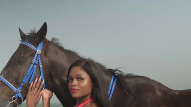 Kırmızı elbiseli genç esmer bir kadın okyanus kıyısında bir atın yanında duruyor. Yavaş çekim.