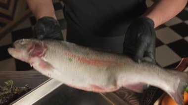 Eldivenli şef, sebze ve otların arasında bir masada duran bir tepsiye balık atıyor. Yavaş Hareket, Kapat.