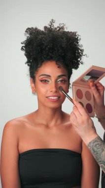 Dubai, BAE - 710 2023: Profesyonel makyaj ustası kıvırcık saçlı genç bir modele boya uyguluyor. Dikey, Yavaş Hareket, Kapat.