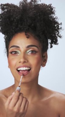 Kasvetli saçı ve parlak makyajı olan genç bir mankenin dikey portresi. Rujlu boya küpleri. Yavaş Çekim, Yakın Çekim. Stüdyo çekimi.