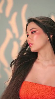 Rüzgarda savrulan uzun saçlı ve parlak makyajlı genç bir kadının dikey portresi. Yavaş Çekim, Kapat, Stüdyo Çekimi.