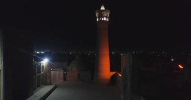 Karmaşık Kalyan Minaresi 'nin aydınlatılmış antik kulesinin yakınında bir dron gece uçar. Buhara, Özbekistan, Havadan görünüm.