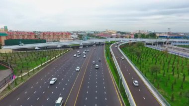İnsansız hava aracı hareket halindeki arabalarla şehrin yollarında ve otoyollarında uçuyor. Bulutlu bir yaz günü. Hava Görünümü.