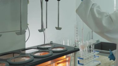 Koruyucu giysiler içindeki laboratuvar teknisyeni laboratuardaki otomatik karıştırıcıdan kimyasal örnekler alıyor. Kapat, Yavaş Hareket.