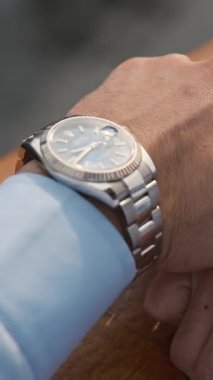 Lüks kol saati olan iş elbiseli genç bir adam pahalı bir premium arabanın yanında duruyor. Dubai 'de bulutlu bir akşam. Kapat, Yavaş Hareket