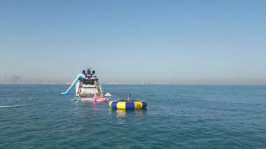 Dubai, BAE - 320 2023: İnsansız hava aracı jet ski kullanan insanların üzerinde uçuyor ve arka planında Dubai olan bir yatın etrafında elektrikli folyo var. Hava Görünümü, Yavaş Hareket.