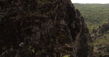 Bir dron, dik bir yamaçta tek kolunda asılı duran genç bir atletik kadın dağcının etrafında uçuyor. Hava Görünümü