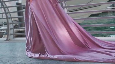 Sarışın ve uzun mor elbiseli genç bir kadın marina boyunca Dubais gökdelenlerinin önünde yürüyor. Yavaş Hareket.