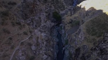 İnsansız hava aracı bir nehirle dağ kanyonunun üzerinden uçuyor. Güneşli bir yaz günü. Hava Görünümü.