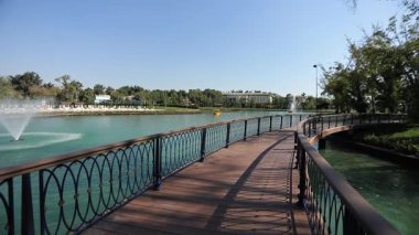 Şehir gölünün üzerinde çeşmelere bakan iskele boyunca bir yürüyüş. Güneşli bir yaz günü. Yavaş Hareket