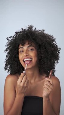 Kasvetli saçı ve parlak makyajı olan genç bir mankenin dikey portresi. Rujlu boya küpleri. Yavaş Çekim, Yakın Çekim. Stüdyo çekimi.