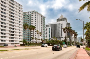 Miami, Florida, ABD - Indian Creek Drive Miami Beach 'in canlı atmosferini gösteren palmiye ağaçlarıyla kaplı modern binalara ev sahipliği yapıyor. Bisikletçiler manzaranın tadını çıkarırken arabalar yolda geziniyor..