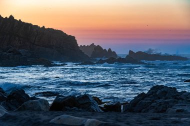 Şili 'de güneş Matanza' nın üzerinde batarken dalgalar kayalık kıyılara çarpıyor, gökyüzünü turuncu ve mor renklerle boyuyor, huzurlu bir sahil kaçışı yaratıyor..