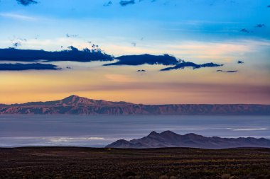 Bu geniş manzara, alacakaranlıkta muazzam Atacama Tuz Düzlüğü 'nü yakalar, canlı gökyüzü ve uzak dağlarla kuzey Şili çölünün dingin güzelliğini vurgular..