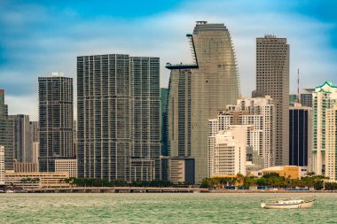 Miami 'nin şehir merkezinin göz kamaştırıcı manzarası ve açık mavi gökyüzünün altındaki tuğlalı bölge. Şehrin dinamik büyüme ve mimari çeşitliliğini gösteren parlak gökdelenler su üzerinde yükseliyor..