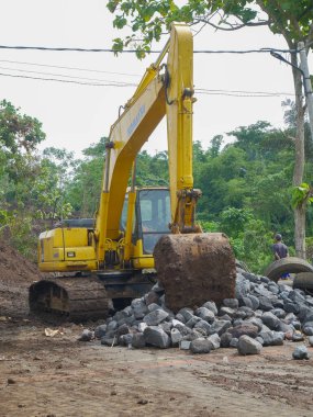 Malang, Indonesia -January 22, 2023 : Big yellow excavator digging construction site for building. the size of an excavator compared to a human