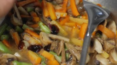 Kızarmış sebzeleri spatula kullanarak tavada pişirme işlemi. İçinde havuç, mantar ve yeşil hardal bulunan kızarmış sebzeler.