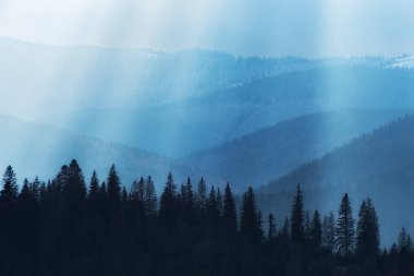 Sunrays from clouds shining down to mountains. Sun rays over valley.  Silhouettes of trees on the mountains.