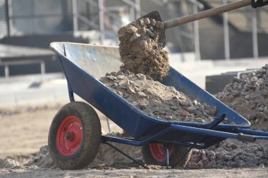 Çakıl taşlı el arabası. İnşaat alanındaki işçiler taşı el arabasına kürekle dolduruyorlar..