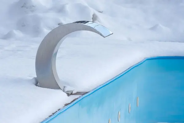 Empty swimming pool in winter, covered with snow.
