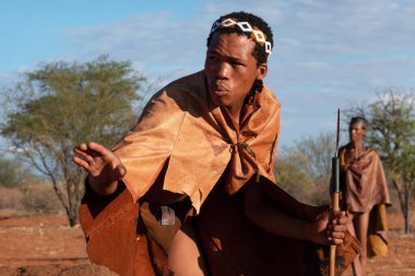 KALAHARI DESERT, NAMIBIA - 17 Kasım 2024: Kalahari Çölü 'nün kırmızı kumlarındaki Bushmen kabilesi üyeleri, Namibya, Afrika. Buşmen kabileleri hala Kalahari Çölü 'nde yaşıyor ve geleneksel mesleklerini sürdürüyorlar: göçebe yaşam tarzı, Hunti.