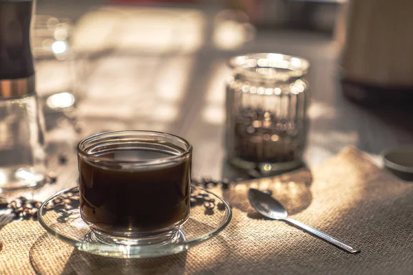 Hot coffee in a clear coffee cup and coffee beans on old wooden in a warm light on top view