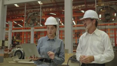 Makinelerle çalışmanın güvenliği, iş akışı bakımı, depolama ve onarım konularını büyük sanayi tesislerinde erkek mühendislere açıklayan kadın mühendis..