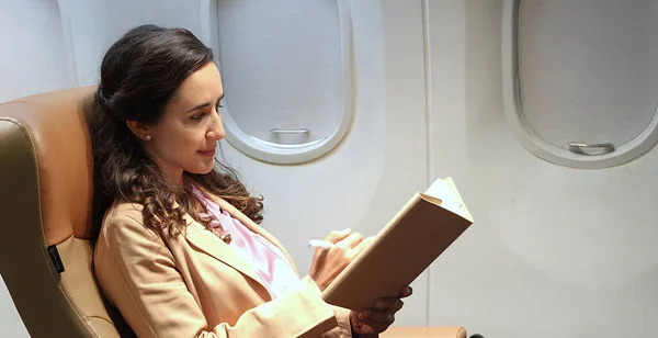 Business woman sitting and writing information in a notebook while sitting on an airplane
