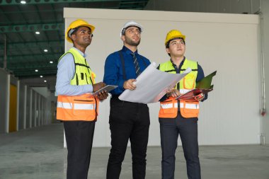 Bir endüstriyel inşaat alanının planlarını inceleyen sağlam şapka ve yelekli çeşitli inşaat mühendisleri..