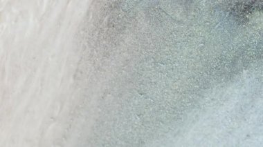 Soyut sıvı sanat arka planı. Bir akarsu akıntısı, parlayan karanlık su. Işıldayan bej ve turkuaz rengi pullar ve mor boya. Yanardöner inci parçacıklarının akışkan hareketinin makro videosu