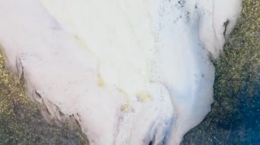 Boşluğu dolduran hızlı bir beyaz boya akıntısı. Soyut sanat. Mavi ve altın kumda ışıltı ve parıltılarla akan sıvı taşkınlığı. Sütlü suyun yakın çekim hareketi. Yüksek kalite