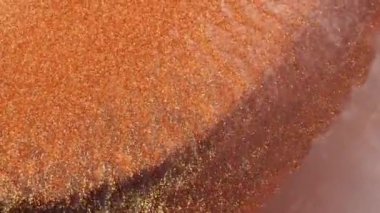 Beyaz alkol mürekkebi turuncu, bronz ve pembe arka plandan aşağı doğru akar. Dalgalanan parlayan yüzey.