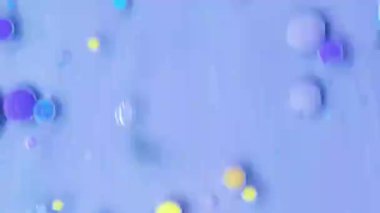 Sarı, mavi ve mor renkli canlı akrilik boya damlaları yatıştırıcı mor bir arka planda yağla nazikçe etkileşime girer ve sanatsal bir ekranda büyüleyici desenler ve dokular yaratır..