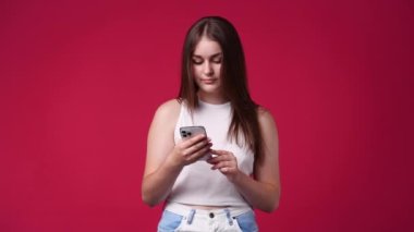 Kırmızı arka planda izole edilmiş telefonu kullanan hoş bir kadının 4K videosu. Teknoloji kavramı.
