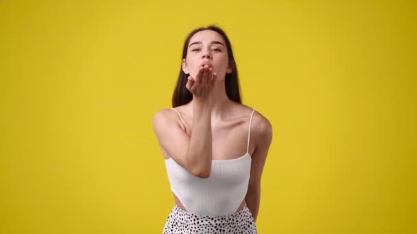 黄色い背景の上に隔離されたキスを送る笑顔の女性の4Kビデオ 空気キスの概念 — ストック動画