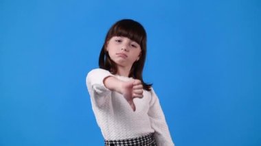 Küçük kızın mavi arka planda başparmağını gösterdiği 4K video. Olumsuz duygu kavramı.