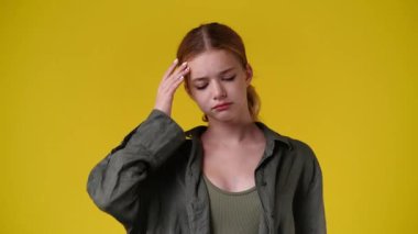 Üzgün kızın sarı arka planda alnına dokunduğu 4k 'lık video. Duyguların kavramı.