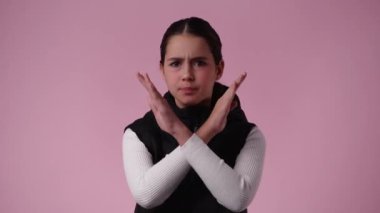 Pembe arka planda çapraz elleri olan bir kızın 4K videosu. Olumsuz duygu kavramı.