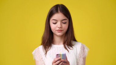 Sarı arka planda telefonunu kullanan bir kadının 4K videosu. Duygu kavramı.
