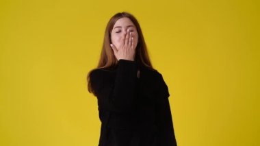 Sarı arka planda hava öpücüğü gönderen bir kızın 4K videosu. Aşk duygusu kavramı.