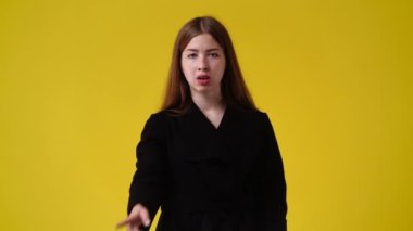 Sarı arka planda sessizlik işareti gösteren bir kızın 4K yavaş videosu. Duyguların kavramı.